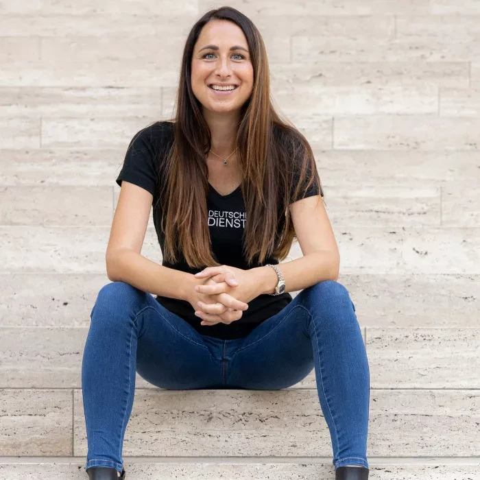 A smiling woman sits on stone steps, wearing a black T-shirt with the words "Company Bikes" and blue jeans.