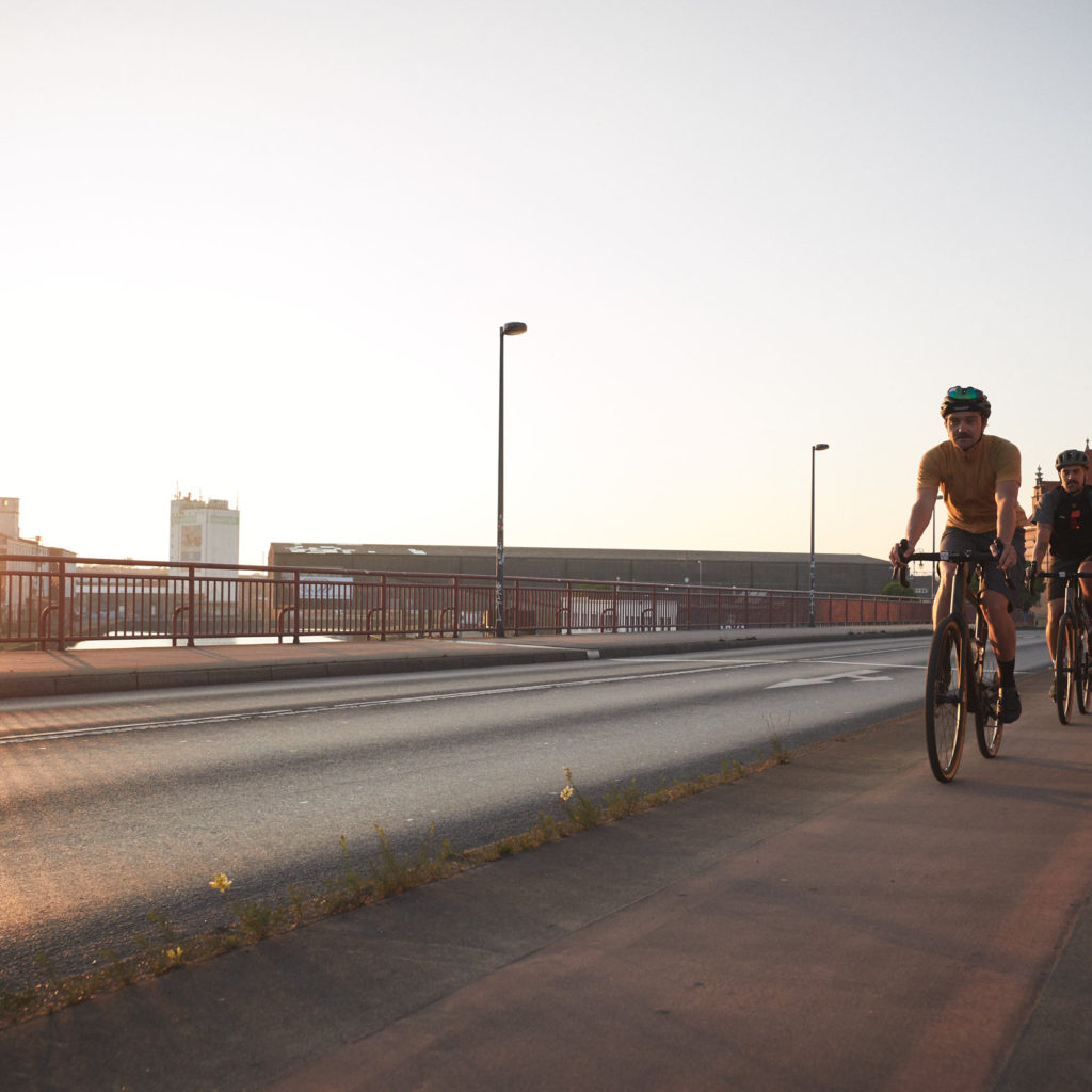 Two cyclists ride across a bridge at sunrise or sunset.