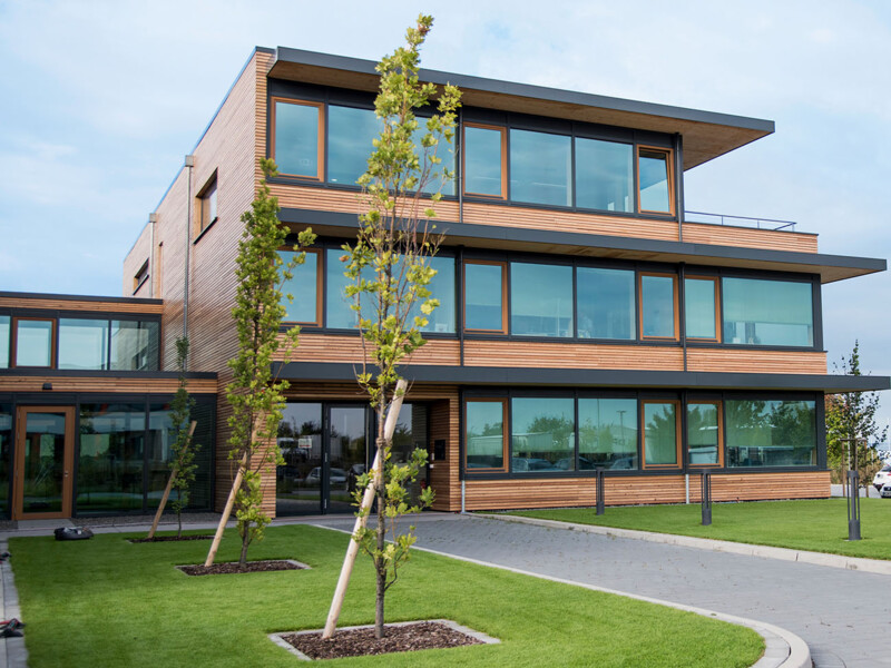 Modern building with wood paneling, large glass windows, and green lawn in the foreground.