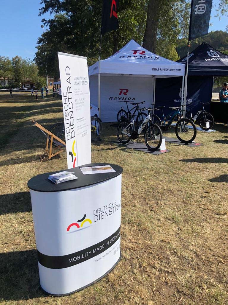 An outdoor exhibition stand for "Deutsche Dienstrad," surrounded by bikes and pavilions from various brands.