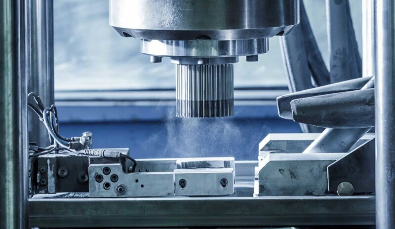 Close-up of an industrial machine processing or pressing a piece of metal, surrounded by metal parts and technical components.